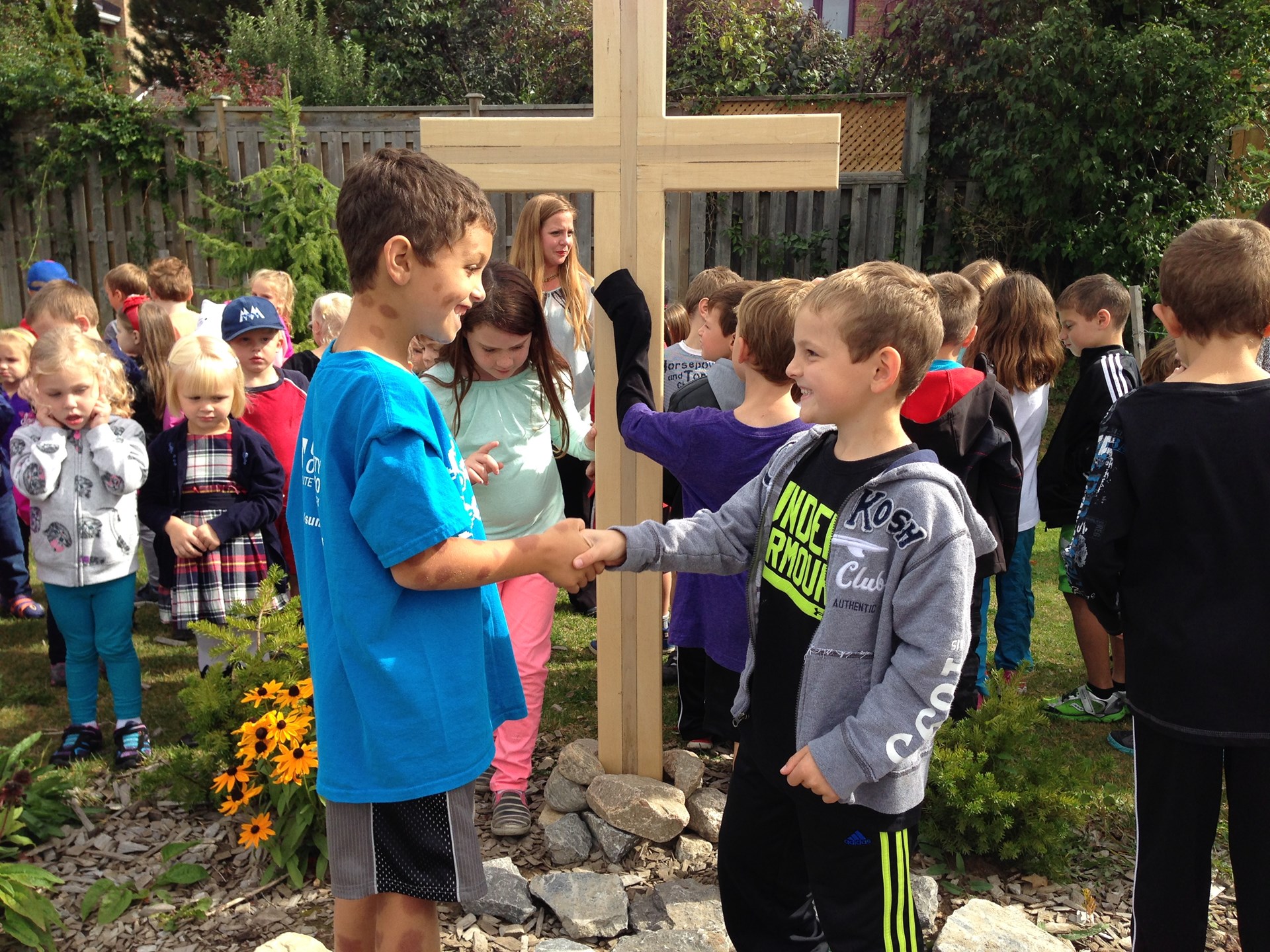 Students shaking hands in front of cross outside.